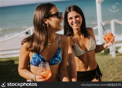 Two smiling young women in bikini enjoying vacation on the beachwhile drinking cocktail