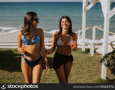 Two smiling young women in bikini enjoying vacation on the beachwhile drinking cocktail