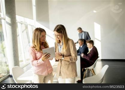 Two smiling young women looking on digital tablet at the office