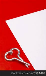 Two spiral bolts laying in the form of heart on a red background near to a leaf of a paper. Steel heart with mark