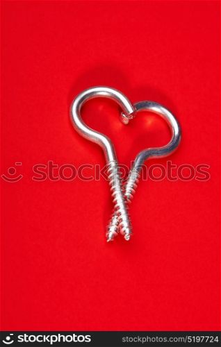 Two spiral bolts laying in the form of heart on a red background. Steel heart