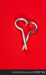 Two spiral bolts laying in the form of heart on a red background. Steel heart