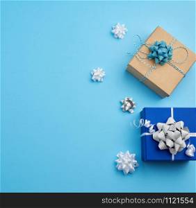 two square gift boxes decorated with ribbons and bows on a blue background, top view, place for text