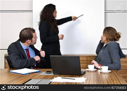 Two staff members paying attention to a team leader, pointing to items on a presentation screen