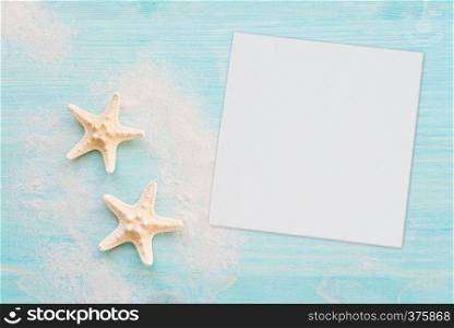 Two starfishes and white sea sand are on the background of blue faded wooden deck. Marine concept