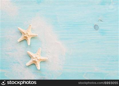 Two starfishes and white sea sand are on the background of blue faded wooden deck. Marine concept