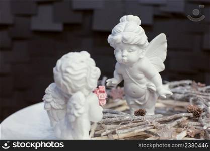 two statues of angels with wings and a wreath of twigs on a dark background for Christmas. angel figurine from porcelain