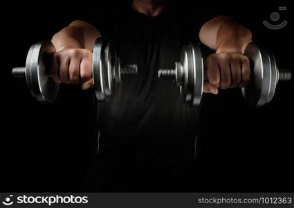 two steel typesetting dumbbells in male hands, arms extended forward and muscles tense, sports backdrop, low key