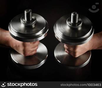 two steel typesetting dumbbells in male hands, sports backdrop, low key