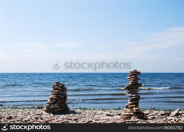 Two stone sculptures by the coast with waves and blue water