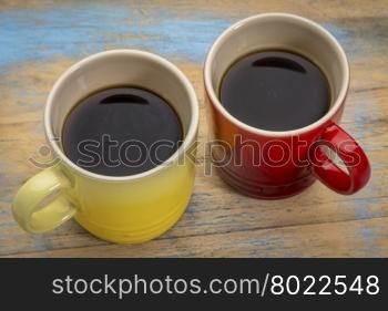 two stoneware cups of espresso coffee against grunge painted wood