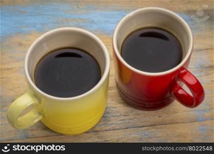 two stoneware cups of espresso coffee against grunge painted wood