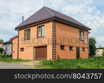 Two-storeyed orange brick cottage with garage, sunny summer day