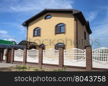 Two-storeyed yellow brick cottage with white concrete fence, sunny day