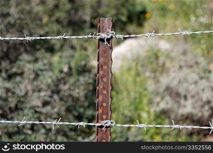 Two strands of barbed wire fence on rusty steel post
