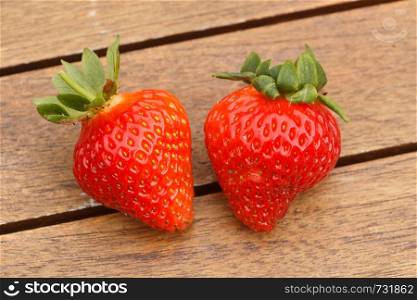 Two strawberries with their leaves on a wooden table