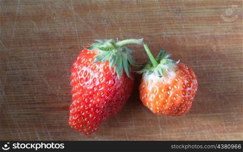 two strawberryes on the wooden plank, horizontal shot, orange and red colors