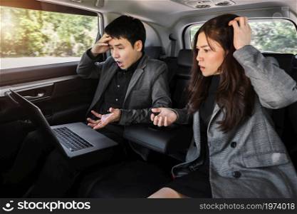 two stressed business man and woman working with laptop computer while sitting in the back seat of a car