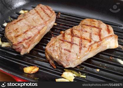 Two striploin (or New York) steaks grilling in a pan with garlic and rosemary