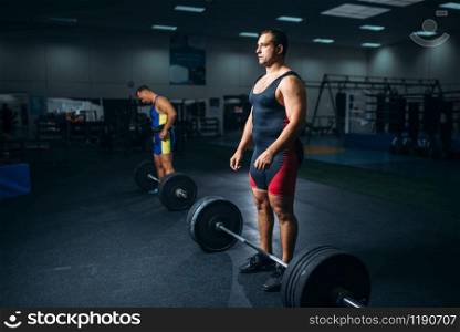 Two strong weightlifters doing exercise with barbells, gym interior on background. Weightlifting workout in fitness club, bodybuilding. Two weightlifters doing exercise with barbells