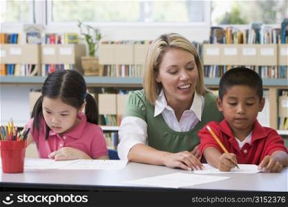 Two students in class writing with teacher helping
