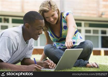 Two students outdoors on lawn with laptop