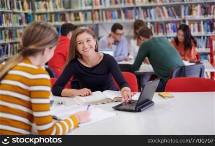 Two students taking notes from a book at library. Young two woman sitting at table doing assignments in college library.