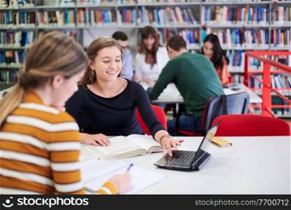 Two students taking notes from a book at library. Young two woman sitting at table doing assignments in college library.