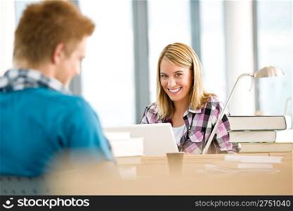 Two students with books and laptop in classroom studying