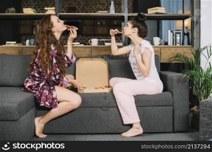 two stylish female friends eating pizza