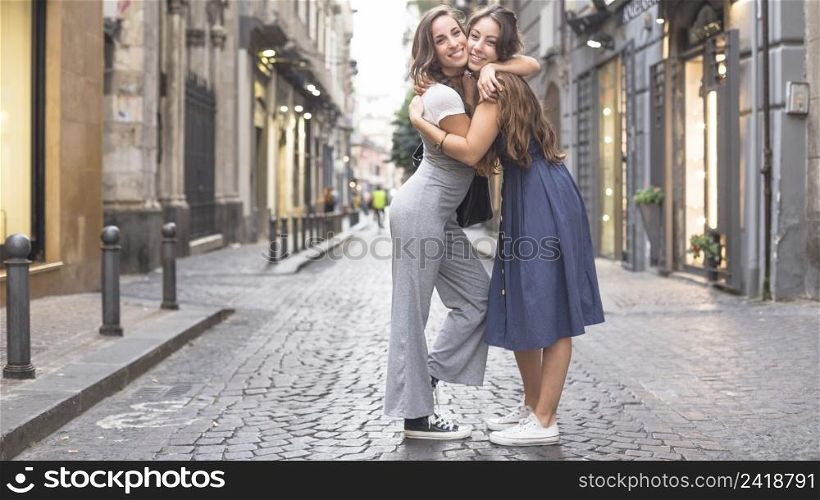 two stylish female friends standing street hugging each other