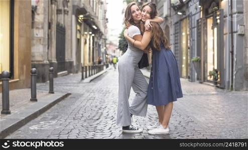 two stylish female friends standing street hugging each other