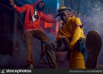 Two stylish rappers dancing in studio with cool underground decoration. Hip-hop performers, trendy rap singers, break-dancers. Two stylish rappers dancing in studio