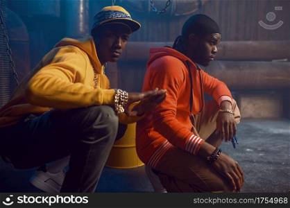 Two stylish rappers poses in studio with cool underground decoration. Hip-hop performers, break-dancers. Two stylish rappers poses in studio