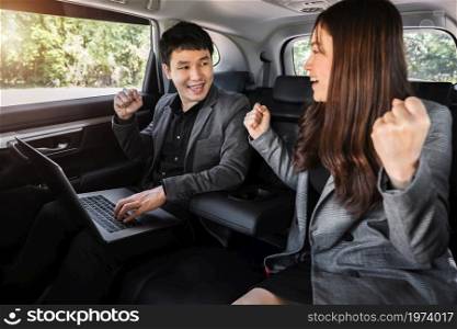 two successful business man and woman working with laptop computer while sitting in the back seat of a car
