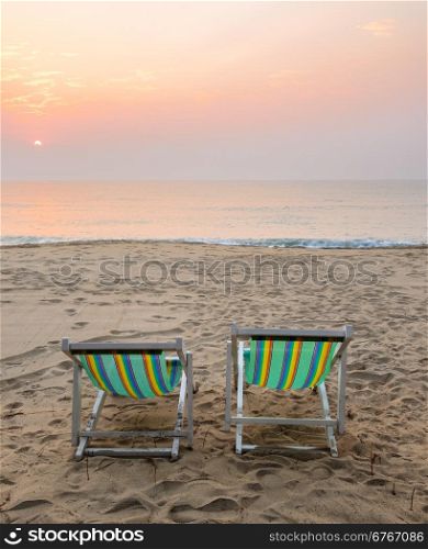 Two sun beach chairs on shore at sunrise in Thailand