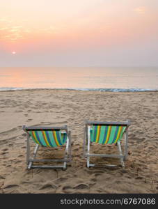 Two sun beach chairs on shore at sunrise in Thailand