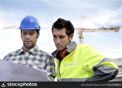two supervisors on a construction site looking at a blueprint