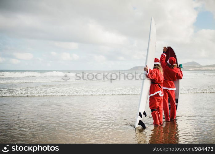 Two surfers dressed as Santa Claus on the beach surfing