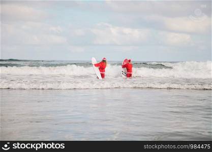 Two surfers dressed as Santa Claus on the beach surfing