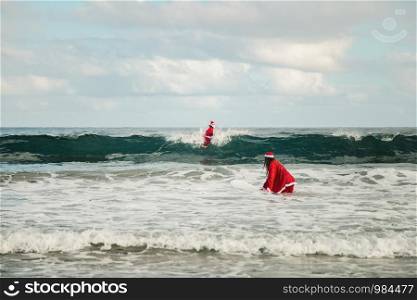 Two surfers dressed as Santa Claus on the beach surfing
