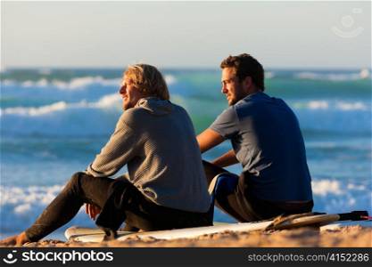 Two surfers sitting on their surf boards on the beach discussing the waves