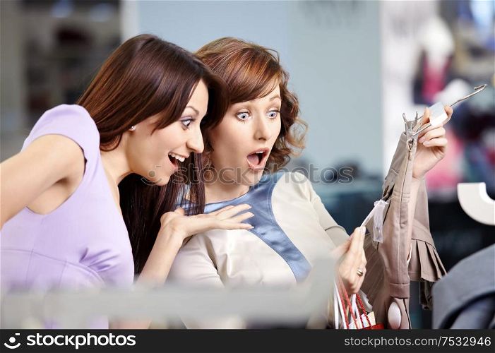 Two surprised girl-friends laugh in clothes shop