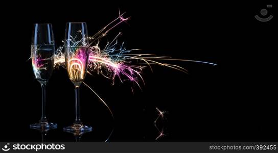 Two tall glasses of champagne against the background of Bengal lights. Black background. The concept of the celebration of the wedding and the new year. Copy space.. Two tall glasses of champagne against the background of Bengal l
