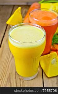 Two tall glasses of pumpkin and carrot juice, chopped vegetables on a wooden boards background