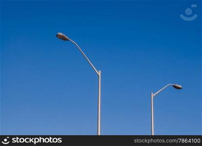 Two tall street lights against clear empty blue sky.