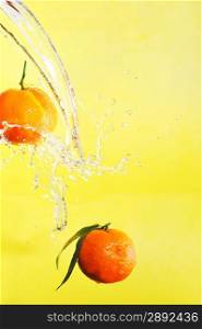 two tangerines and water splashes on yellow, close up