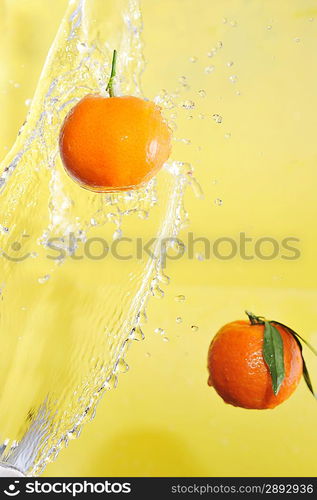 two tangerines and water splashes on yellow, close up