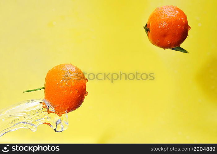 two tangerines and water splashes on yellow, close up