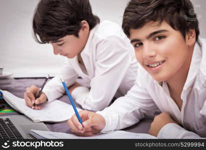 Two teenage boys doing homework at home, writing something in their notebooks, enjoying at school, education concept